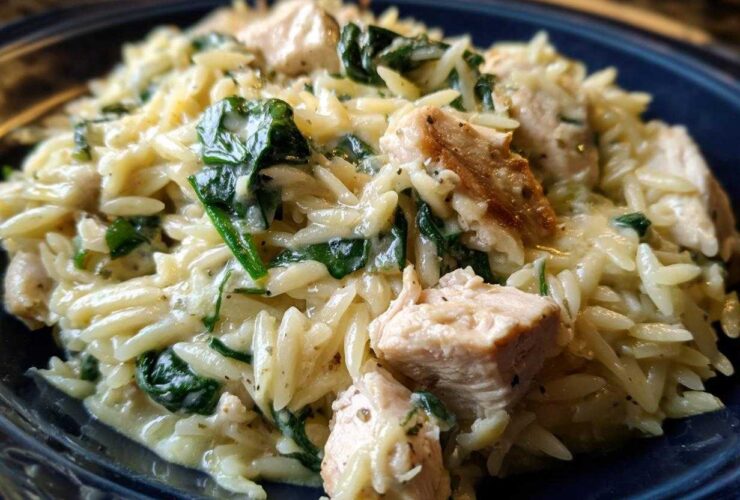 Close-up of creamy lemon chicken orzo mixed with wilted spinach and chunks of seasoned chicken breast.