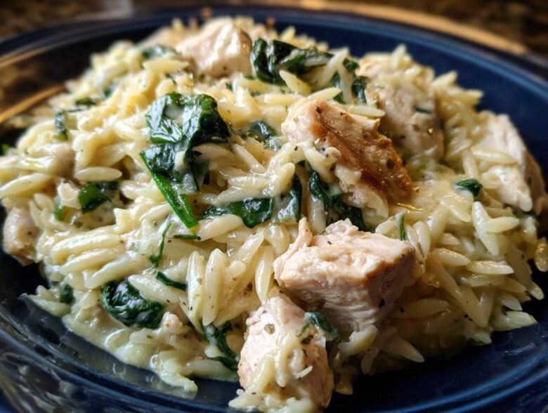 Close-up of creamy lemon chicken orzo mixed with wilted spinach and chunks of seasoned chicken breast.