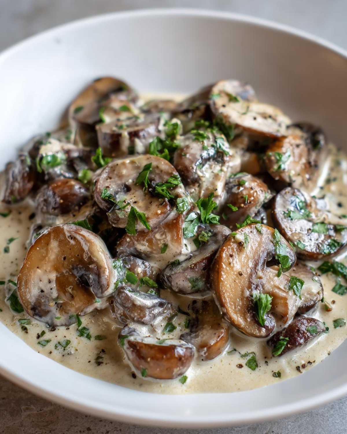 Close-up of rich, creamy mushroom sauce coating sliced brown mushrooms, garnished with fresh parsley.
