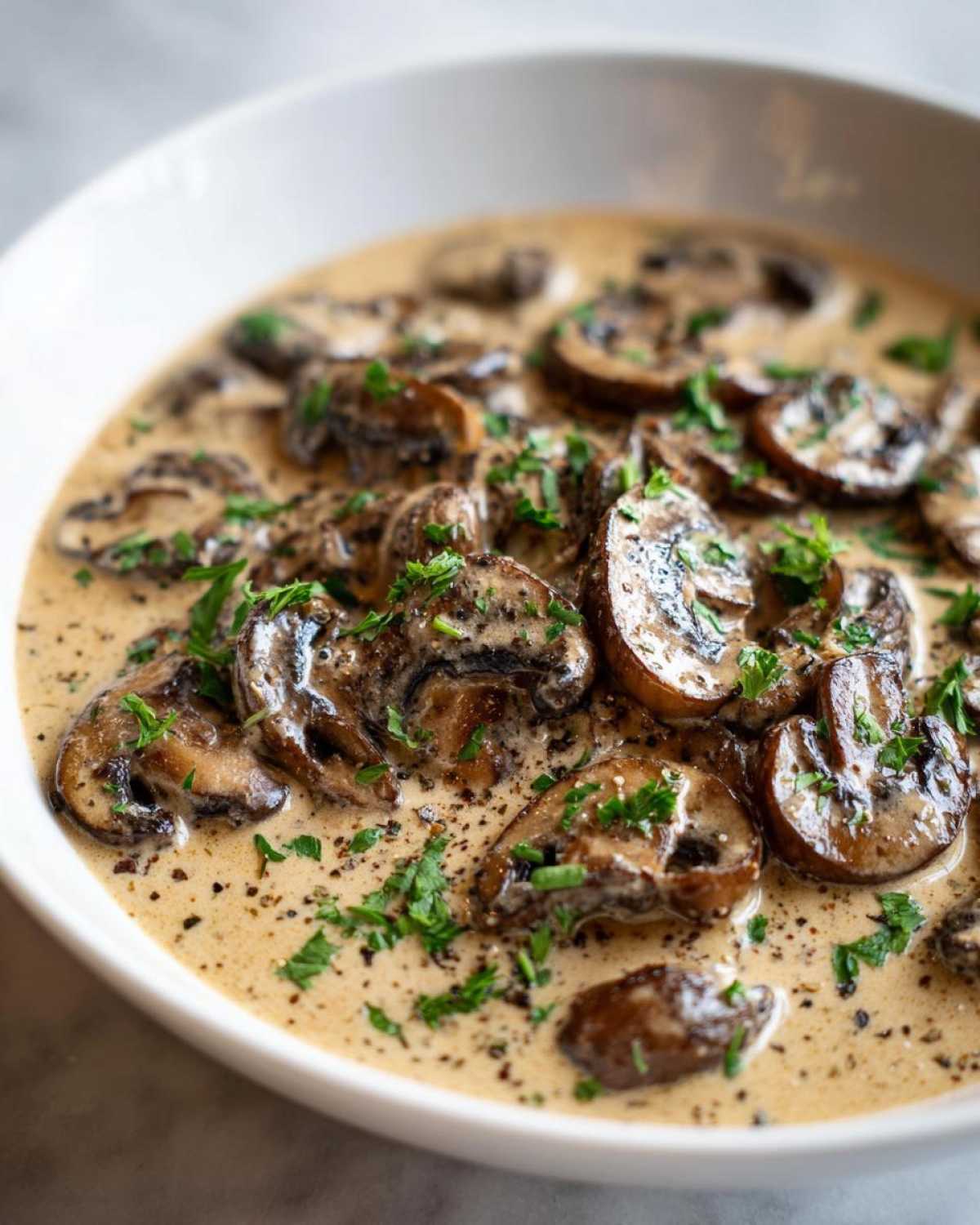 A close-up view of rich, creamy mushroom sauce filled with sliced, sautéed mushrooms and garnished with fresh parsley.
