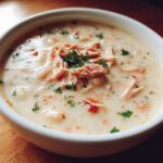 A close-up of a white bowl filled with creamy navy bean soup, topped with shredded meat and fresh parsley.