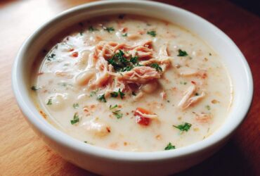 A close-up of a white bowl filled with creamy navy bean soup, topped with shredded meat and fresh parsley.