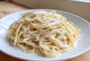 A close-up of creamy parmesan pasta tossed in a rich white sauce and topped with grated cheese and black pepper.