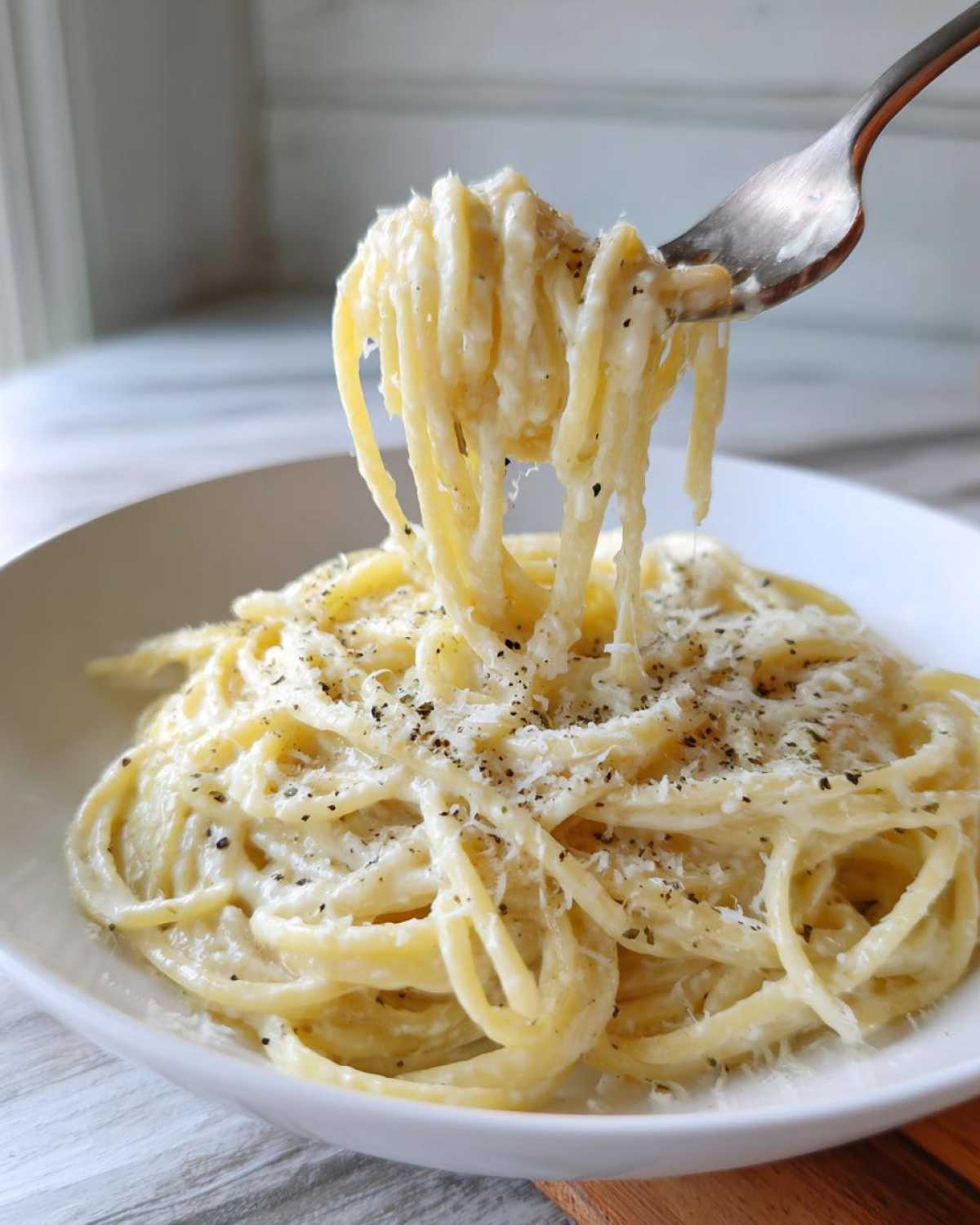 A fork lifting creamy spaghetti coated in sauce from a bowl of amazing parmesan pasta, topped with fresh pepper.