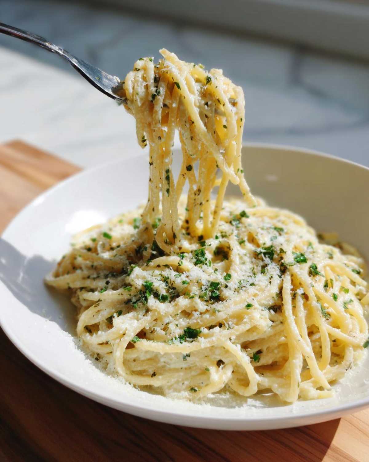 A fork twirls creamy parmesan pasta coated in sauce and topped with fresh parsley.