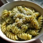 A close-up view of creamy pesto pasta made with fusilli noodles, topped with grated Parmesan cheese.