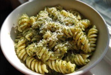 A close-up view of creamy pesto pasta made with fusilli noodles, topped with grated Parmesan cheese.