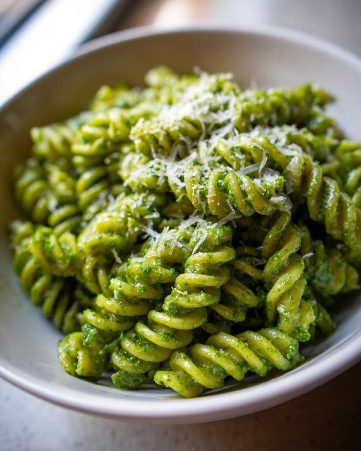 A close-up, appetizing shot of creamy pesto pasta made with fusilli noodles, topped with grated Parmesan cheese.