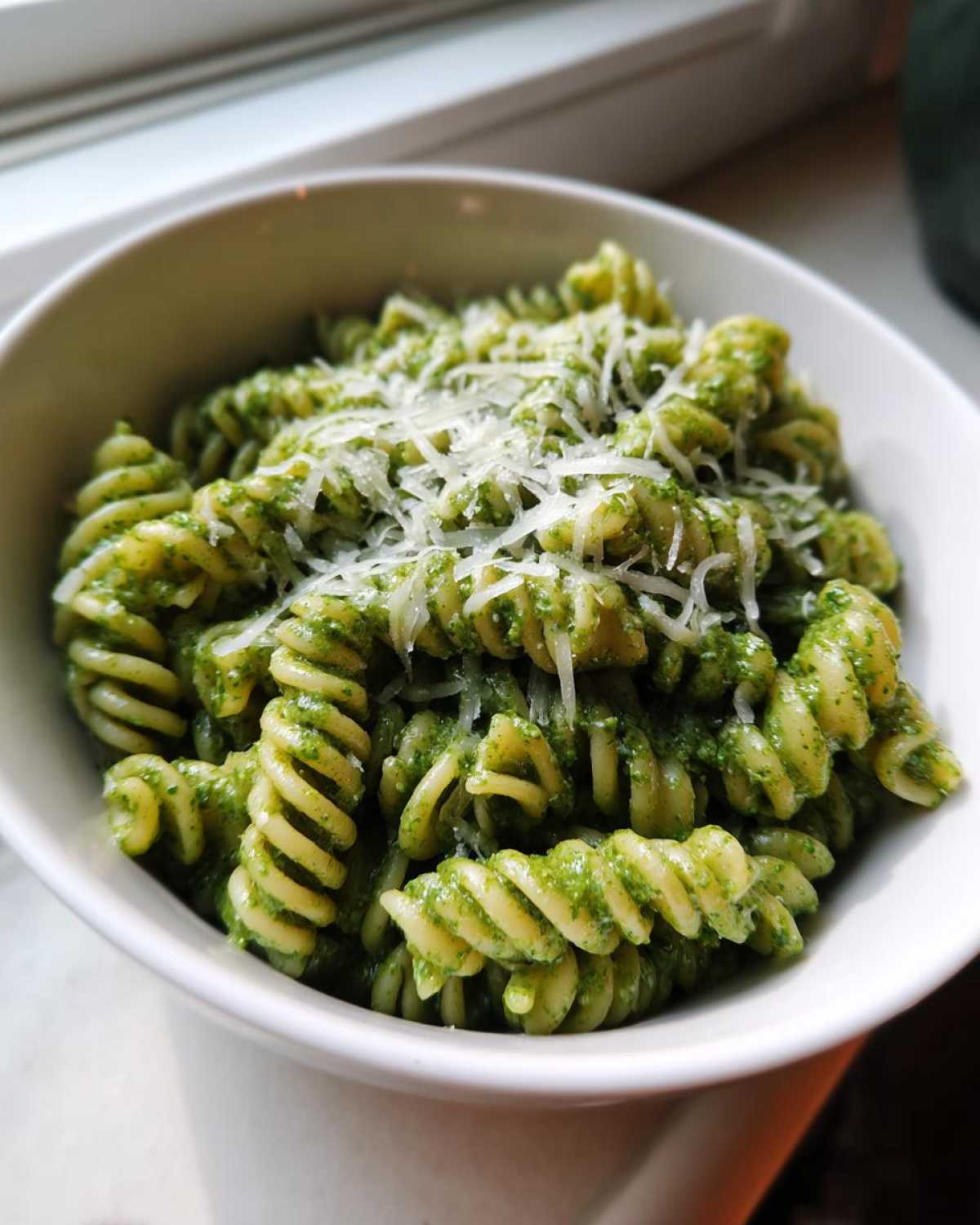 Close-up of creamy pesto pasta made with fusilli noodles, topped with grated Parmesan cheese in a white bowl.