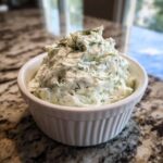 A white ramekin filled with creamy, textured pickle dip, garnished with fresh dill.