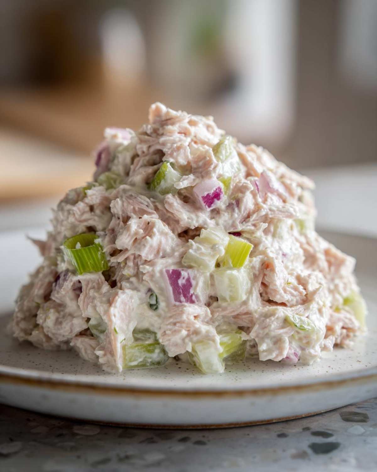 A mound of creamy salmon salad mixed with chopped celery and red onion served on a white plate.