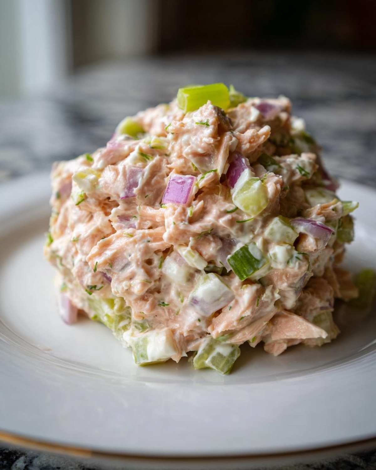 A close-up mound of creamy salmon salad mixed with red onion and celery on a white plate.