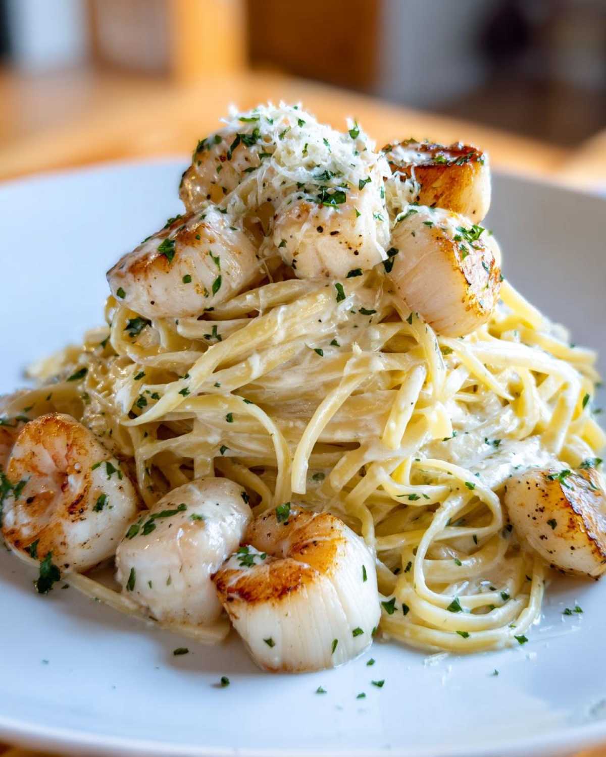 A close-up of creamy seafood pasta topped with perfectly seared scallops and grated cheese.