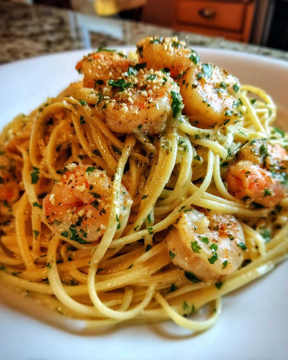 A close-up shot of a serving of creamy seafood pasta topped with perfectly cooked shrimp and fresh parsley.
