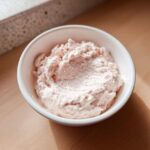 Close-up of a small white bowl filled with creamy, light pink tuna dip, set on a wooden surface.