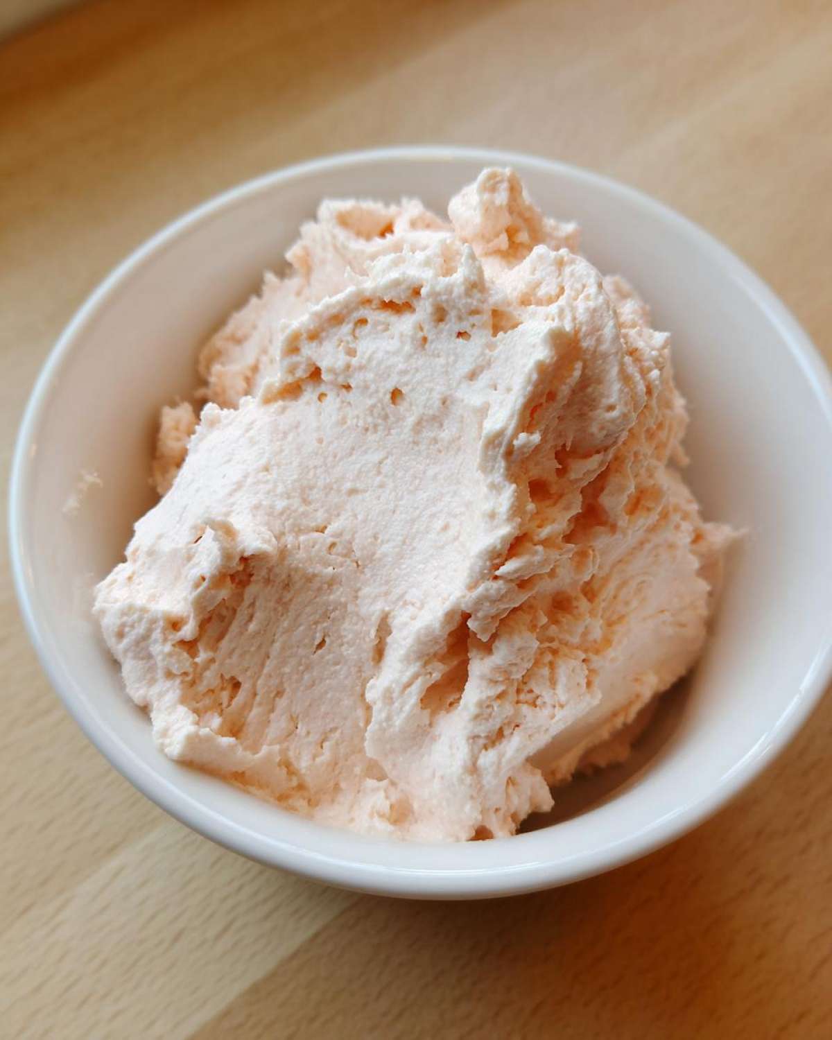 Close-up of a fluffy, pale orange tuna dip served in a small white bowl on a wooden surface.