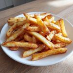 A close-up of golden, crispy air fryer french fries piled high on a white plate, ready to eat.