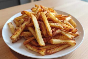 A close-up of a pile of golden, crispy air fryer french fries seasoned lightly and served on a white plate.
