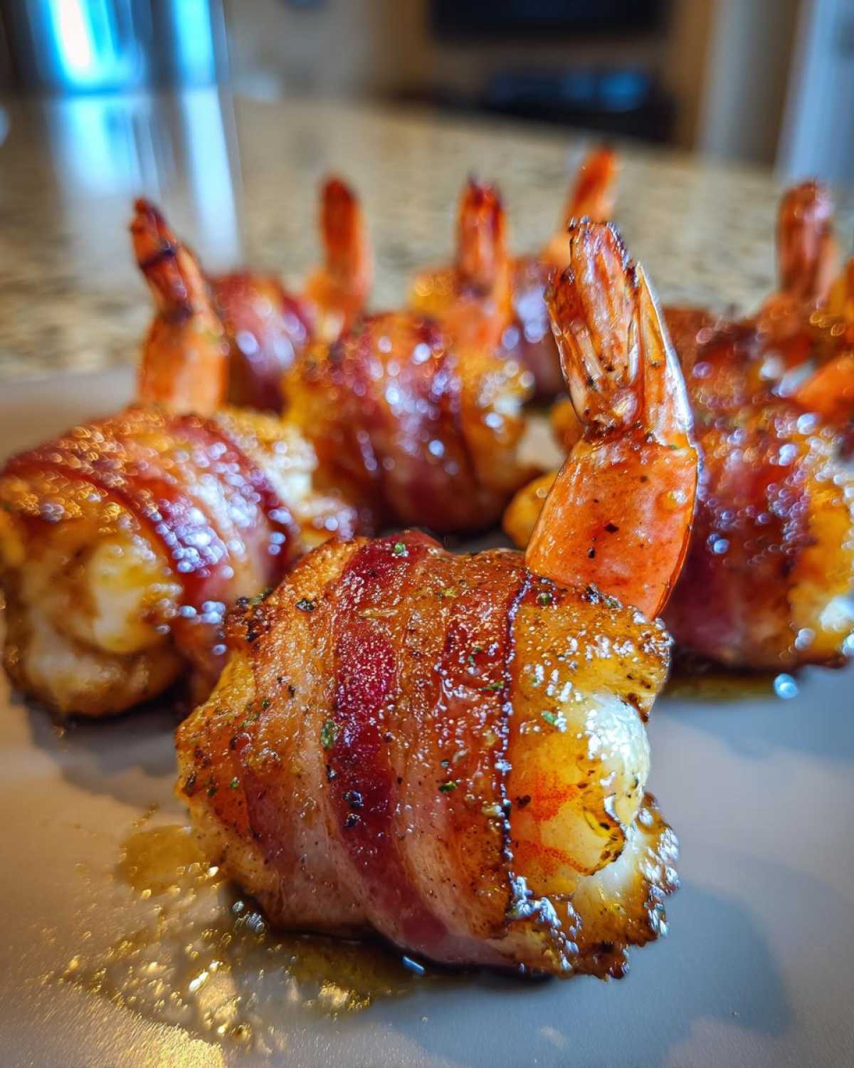 Close-up of perfectly cooked, crispy bacon wrapped shrimp with tails sticking up on a serving plate.