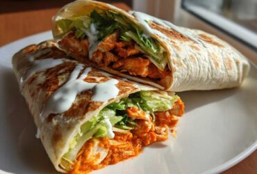 Two halves of a crispy buffalo chicken wrap filled with orange sauce-coated chicken, lettuce, and drizzled with white ranch sauce.