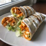 Three delicious buffalo chicken wrap halves stacked on a white plate, showing crispy chicken, lettuce, and ranch dressing.