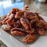 A close-up of freshly made crispy cinnamon sugar pecans piled high on a white rectangular plate.