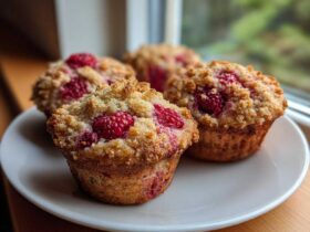 Four golden brown raspberry muffins with a crunchy streusel topping served on a white plate.