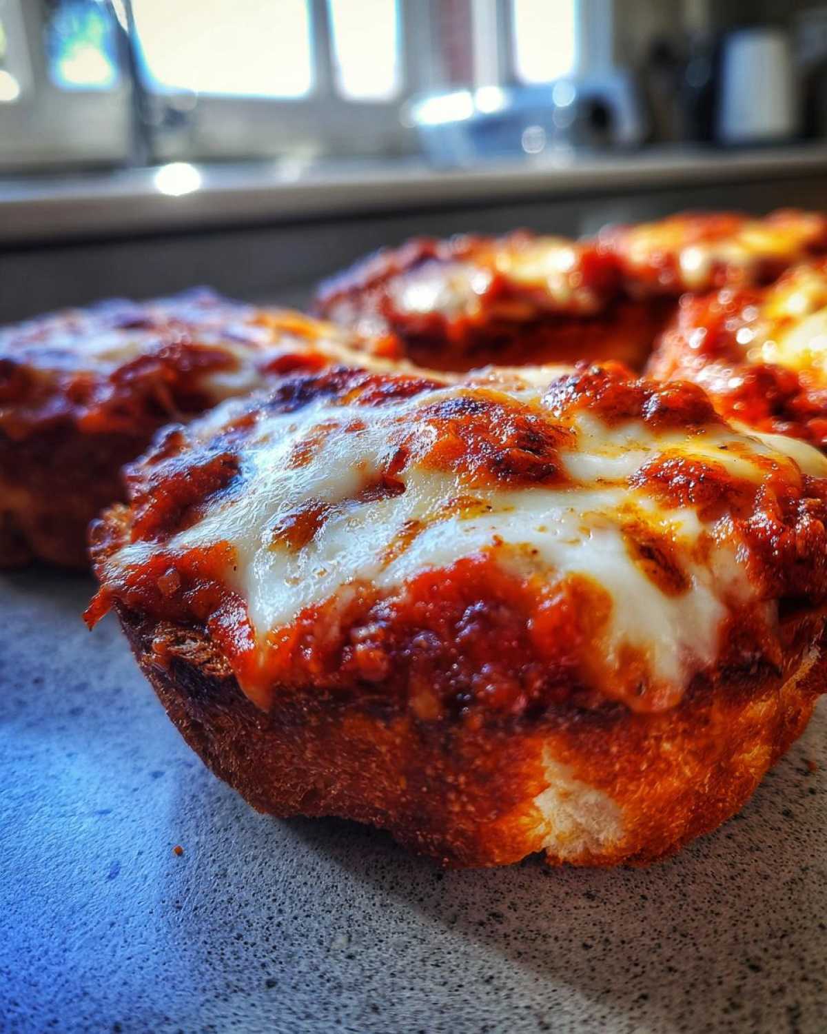 Close-up shot of several hot English muffin pizza halves topped with bubbling tomato sauce and melted mozzarella cheese.
