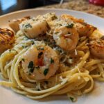 Close-up of a plate of seafood pasta featuring linguine tossed in a light sauce, topped with seared shrimp and scallops, and grated Parmesan.