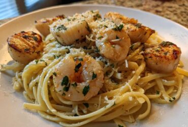 Close-up of a plate of seafood pasta featuring linguine tossed in a light sauce, topped with seared shrimp and scallops, and grated Parmesan.