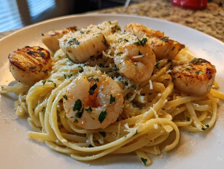 Close-up of a plate of seafood pasta featuring linguine tossed in a light sauce, topped with seared shrimp and scallops, and grated Parmesan.