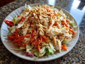 A vibrant plate of thai chicken salad featuring shredded chicken, carrots, cabbage, and topped generously with chopped peanuts.