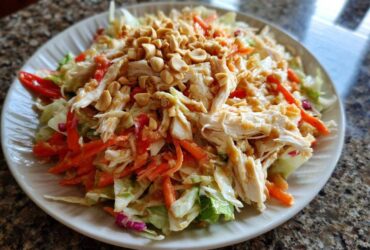 A vibrant plate of thai chicken salad featuring shredded chicken, carrots, cabbage, and topped generously with chopped peanuts.