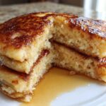 Close-up of fluffy banana pancakes stacked and cut open, showing the airy interior and drizzled with syrup.