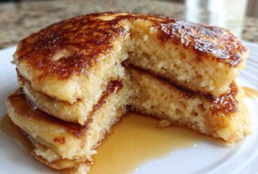 Close-up of fluffy banana pancakes stacked and cut open, showing the airy interior and drizzled with syrup.