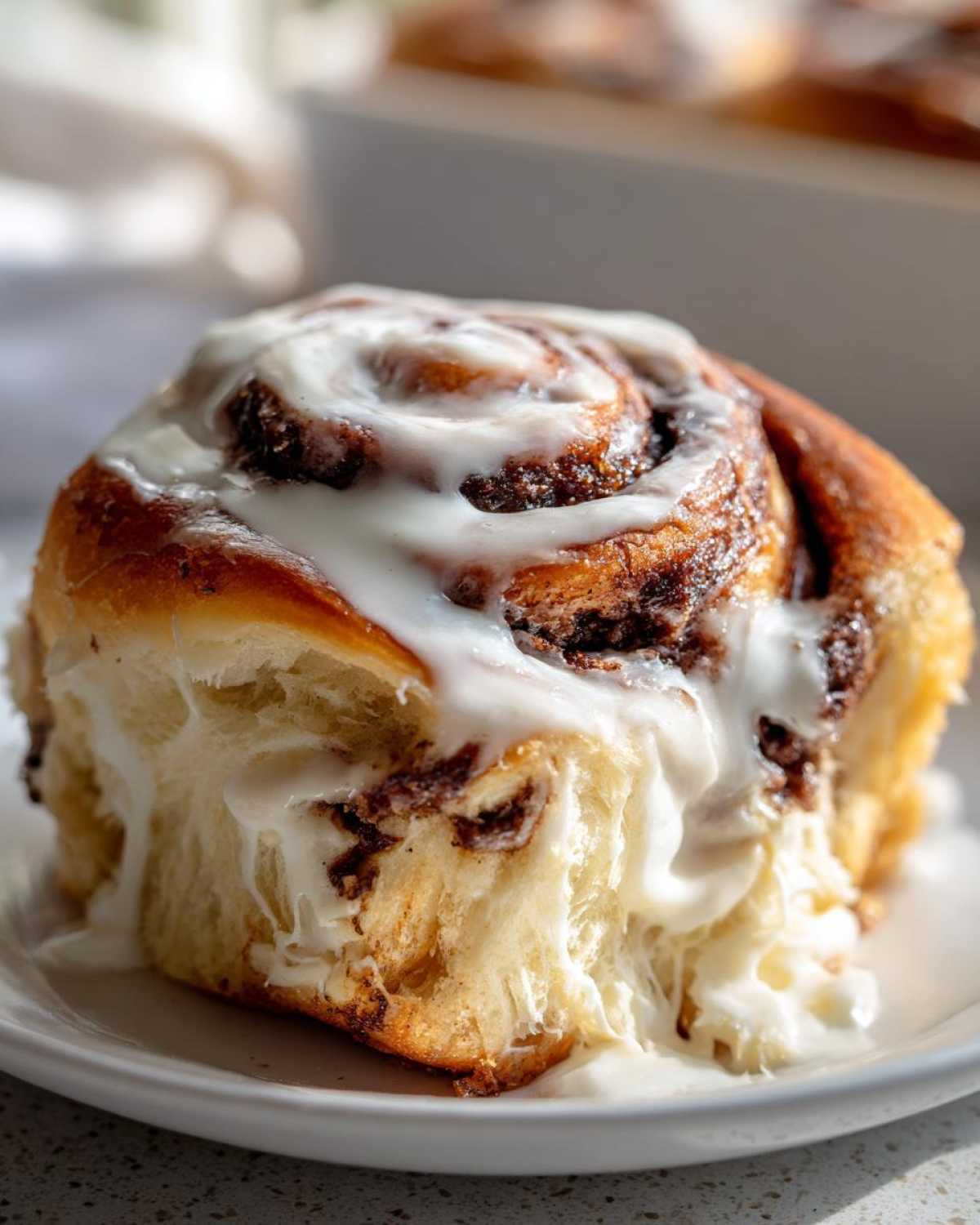 Close-up of a fluffy cinnamon bun dripping with thick, white cream cheese frosting.