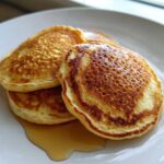 A stack of three fluffy discard pancakes drizzled with maple syrup on a white plate.