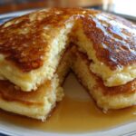 A stack of fluffy discard pancakes cut open, drizzled generously with golden syrup.