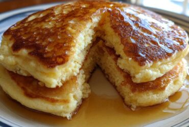 A stack of fluffy discard pancakes cut open, drizzled generously with golden syrup.