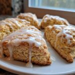 Close-up of several fluffy lemon scones drizzled generously with a tangy white glaze, sitting on a white plate.