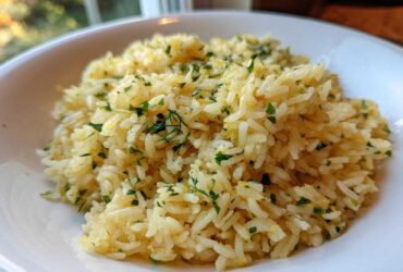 Close-up of fluffy mediterranean rice seasoned with lemon zest and fresh chopped parsley and dill in a white bowl.