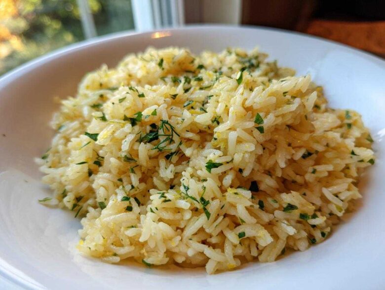 Close-up of fluffy mediterranean rice seasoned with lemon zest and fresh chopped parsley and dill in a white bowl.