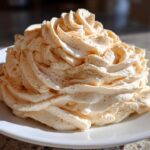 A large swirl of light orange-tinted cinnamon butter, piped high and dusted with ground cinnamon, sits on a white plate.