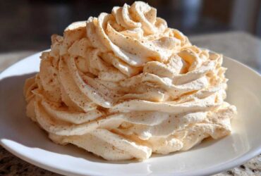 A large swirl of light orange-tinted cinnamon butter, piped high and dusted with ground cinnamon, sits on a white plate.