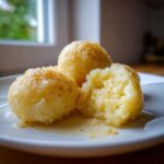 Close-up of fluffy potato dumplings served on a white plate, drizzled with melted butter and spices.