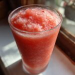 Close-up of a tall glass filled with a bright red, icy frozen strawberry daiquiri.