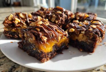A plate of rich, fudgy Turtle brownies layered with gooey caramel, topped with pecans, and drizzled with chocolate ganache.
