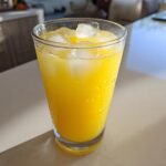 Close-up of a tall, sweating glass filled with bright yellow lemonade and ice cubes.