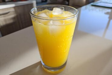 Close-up of a tall, sweating glass filled with bright yellow lemonade and ice cubes.