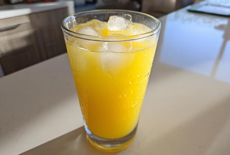Close-up of a tall, sweating glass filled with bright yellow lemonade and ice cubes.